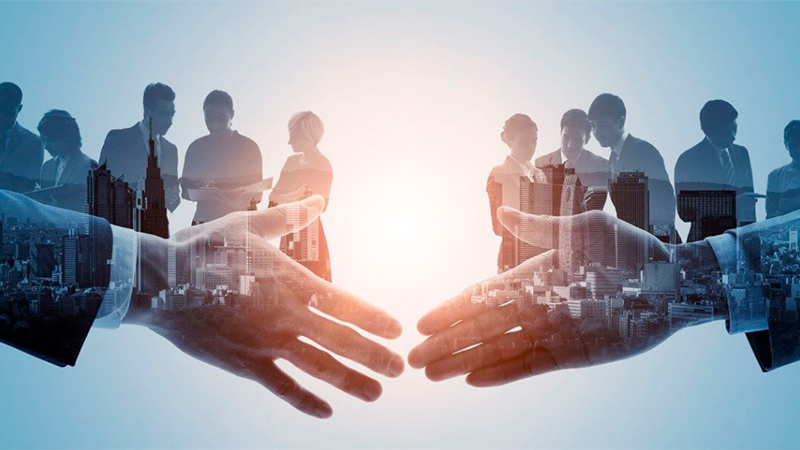 Dois parceiros de negócios apertando as mãos em um escritório moderno com janelas grandes mostrando a cidade, mesa de conferência com laptops e xícaras de café.